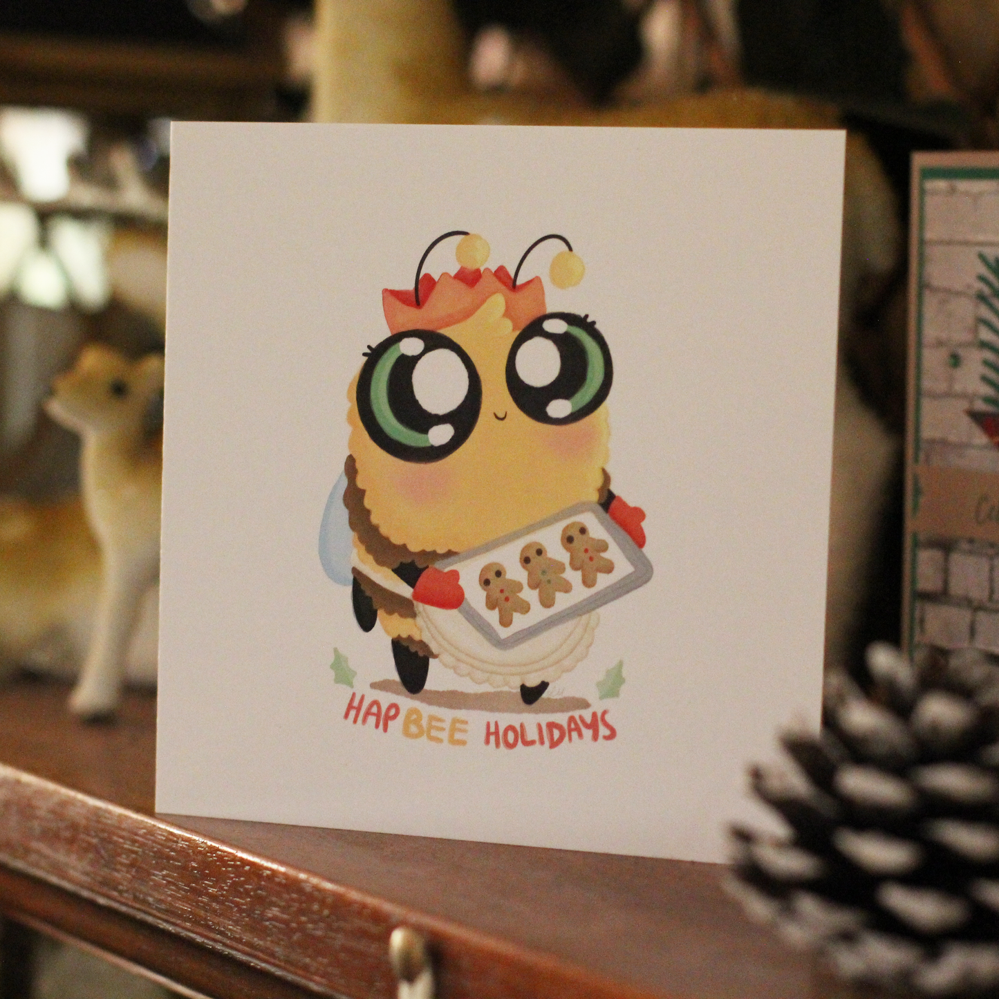 bee themed christmas greeting card sitting on a mantelpiece. The bee is holding gingerbread cookies