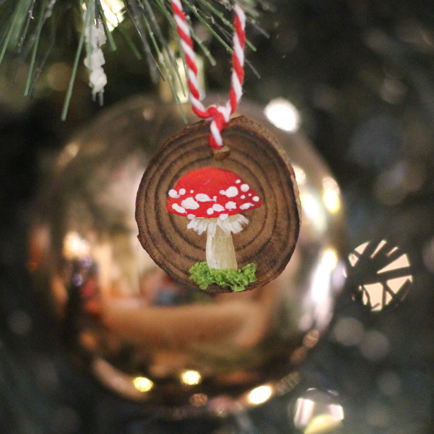 Hand-painted mushroom ornament on a round pinewood disc, with a red and white twine hanger, delicately painted with Amanita Muscaria mushrooms and faux moss.