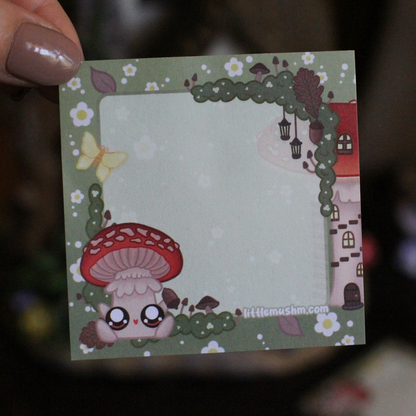 A sticky note with a green background featuring a cartoon mushroom character, flowers, and a small house. The text 'Little mushm' is visible at the bottom.